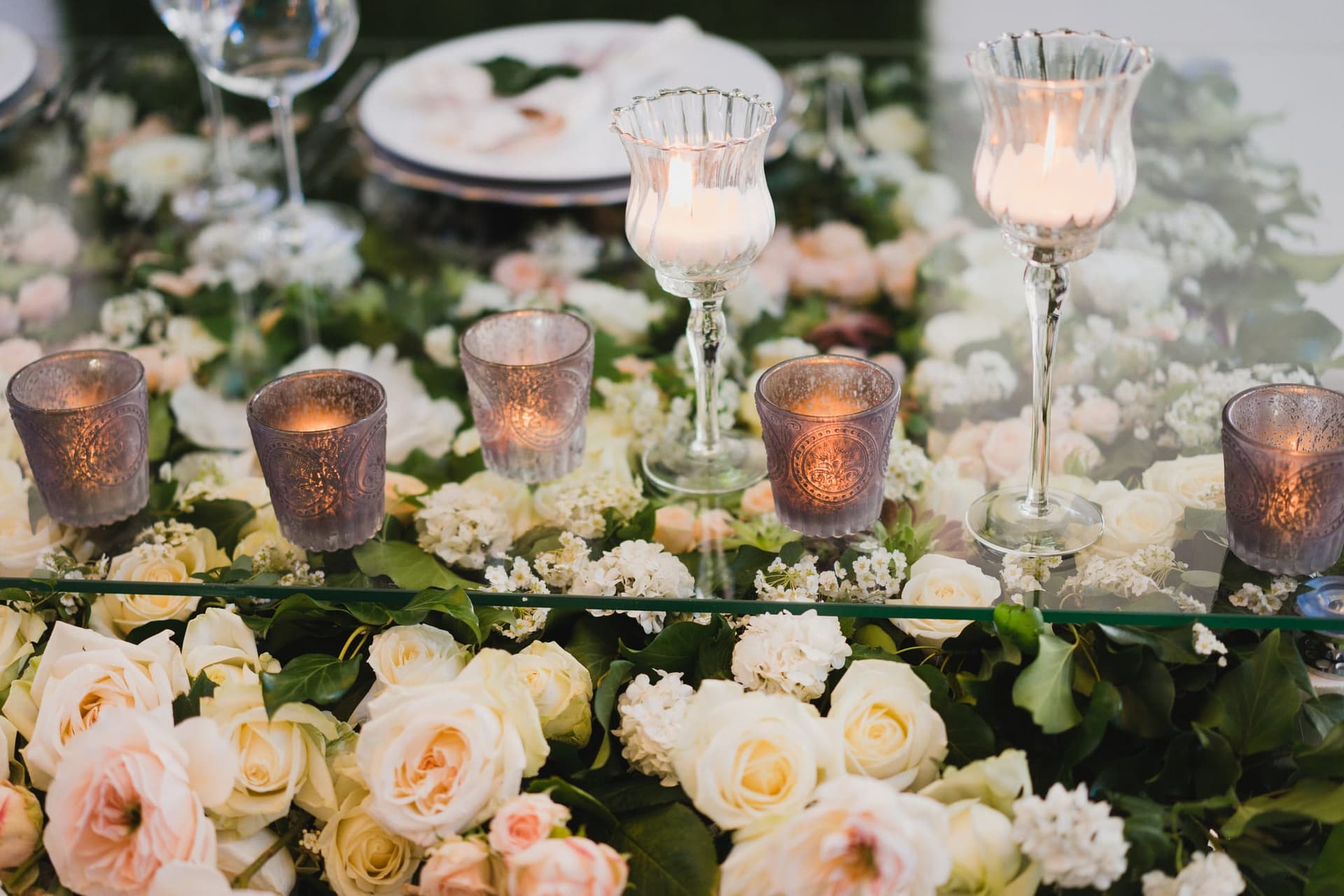 Mesa de boda decorada con flores claras, velas y cristalería